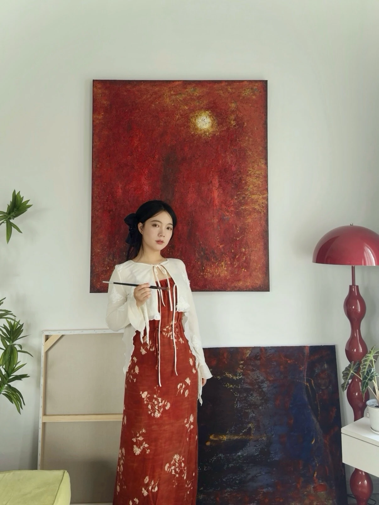 Na Xin holding a paintbrush in front of a red painting.