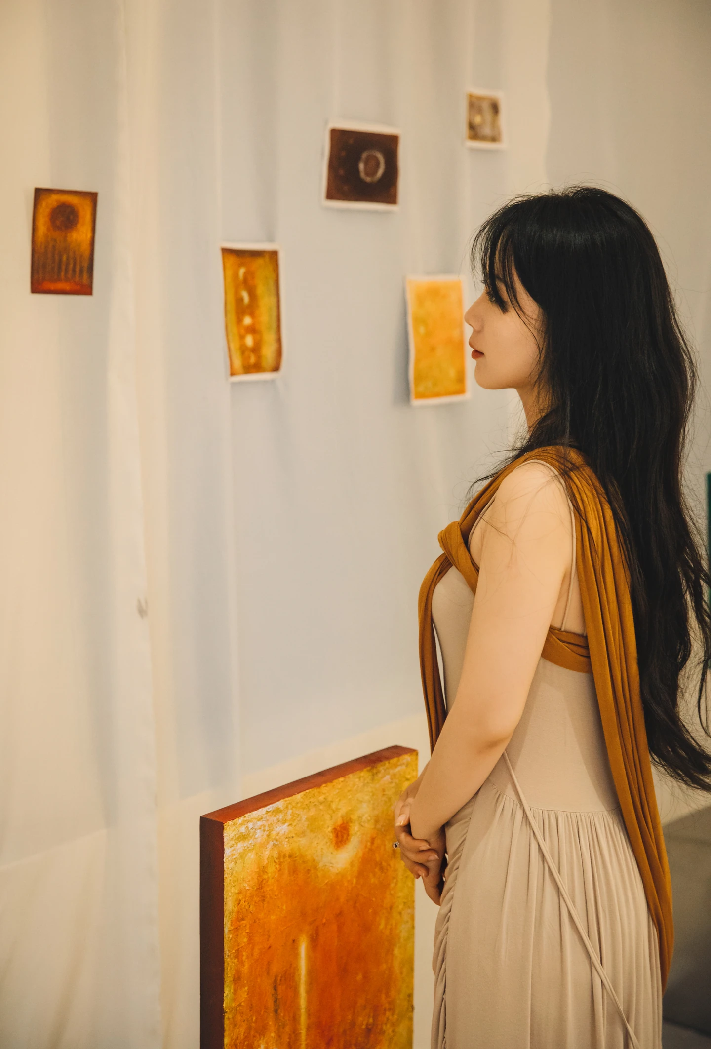Na Xin holding a yellow painting in front of a wall displaying smaller works.